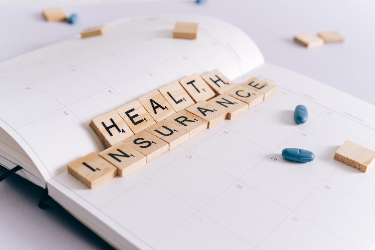 Scrabble tiles spelling 'Health Insurance' on a calendar with pills.